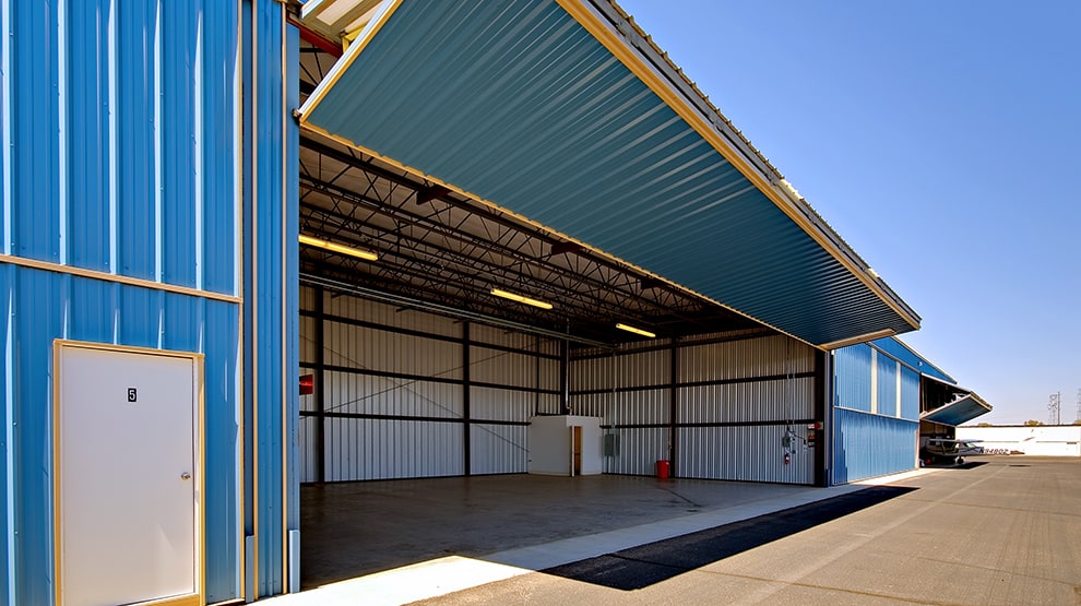 Schweiss custom bifold aviation door with blue and gold colors installed on matching hangar building Schweiss custom bifold aviation door with blue and gold colors installed on matching hangar building