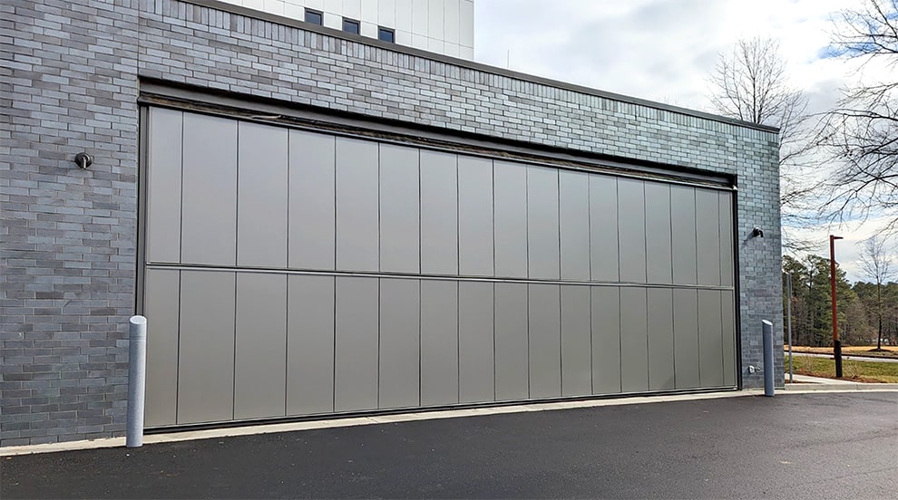 Paneled Schweiss bifold door installed on gray brick building shown closed Paneled Schweiss bifold door installed on gray brick building shown closed