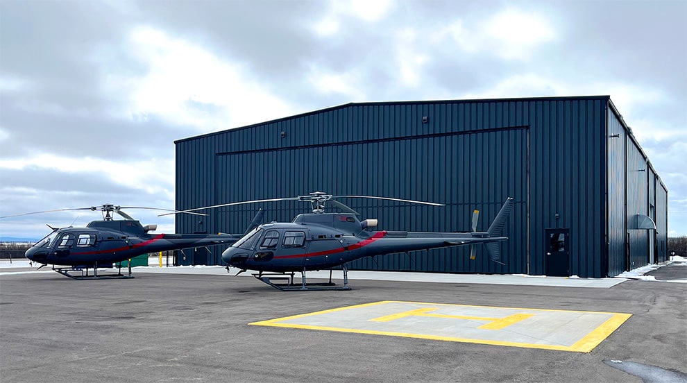 Two helicopters parked in front of a hangar with a Schweiss bifold liftstrap door installed in Calgary, Alberta, Canada Two helicopters parked in front of a hangar with a Schweiss bifold liftstrap door installed in Calgary, Alberta, Canada