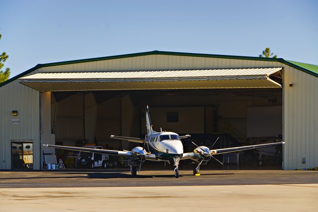airplane parked in front of steel building with large open bifold door.