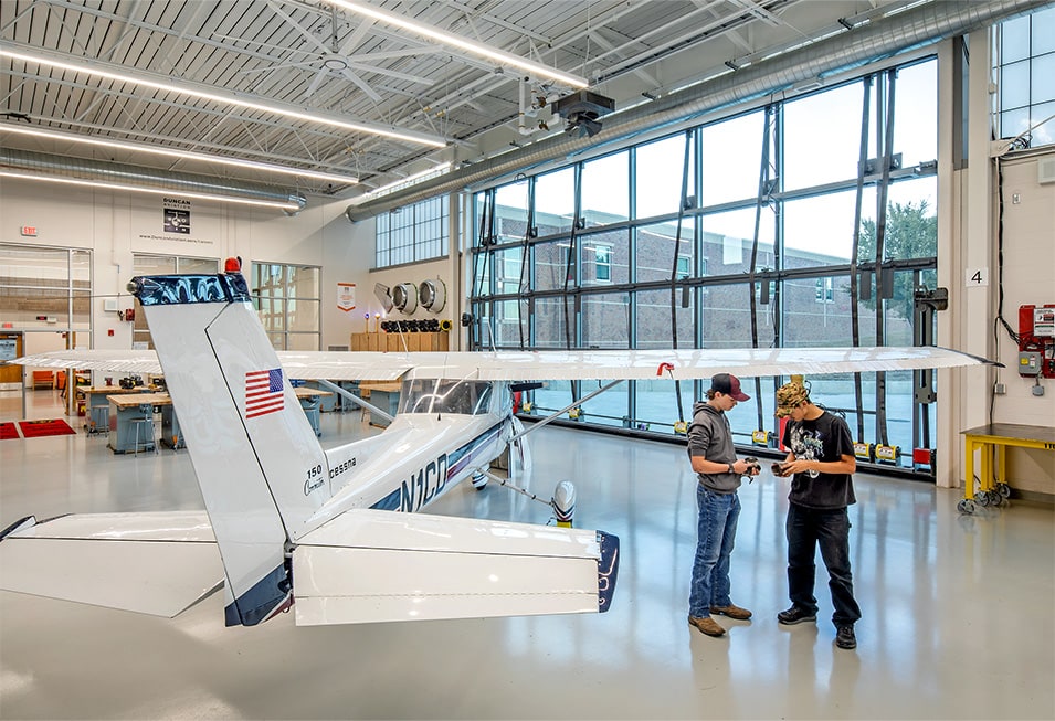 Interior view of Schweiss glass bifold door installed on Lincoln North Star High School behind students and a stored airplane Interior view of Schweiss glass bifold door installed on Lincoln North Star High School behind students and a stored airplane