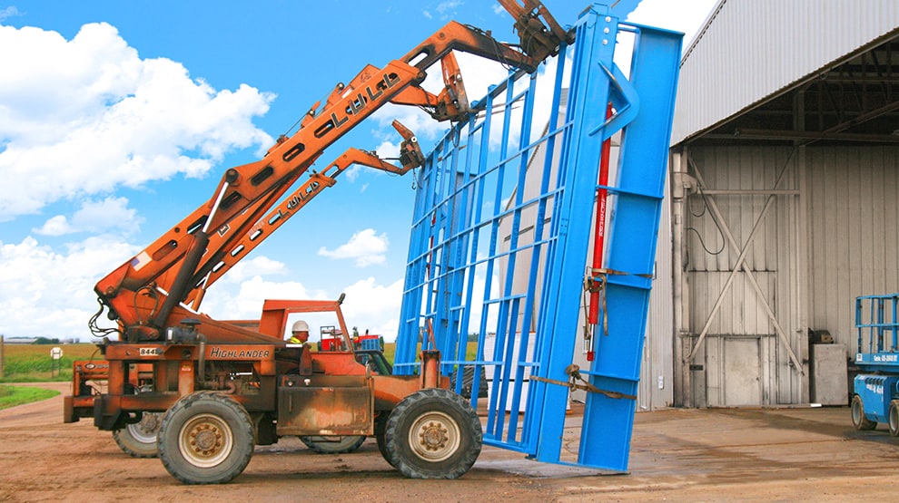 Three telehandlers carrying a large Schweiss stand alone door in preparation to get it installed on building Three telehandlers carrying a large Schweiss stand alone door in preparation to get it installed on building