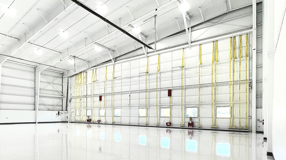 Inside all-white hangar fitted with Schweiss lift strap bifold door shown closed from the right side Inside all-white hangar fitted with Schweiss lift strap bifold door shown closed from the right side
