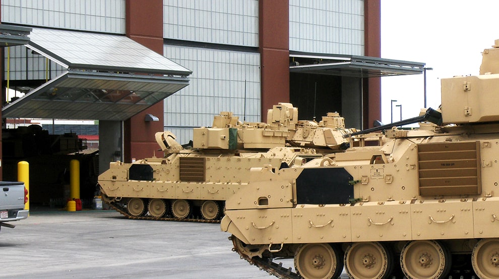 Multiple military tanks parked outside of and driving through Schweiss bifold security doors installed at Fort Carson Multiple military tanks parked outside of and driving through Schweiss bifold security doors installed at Fort Carson