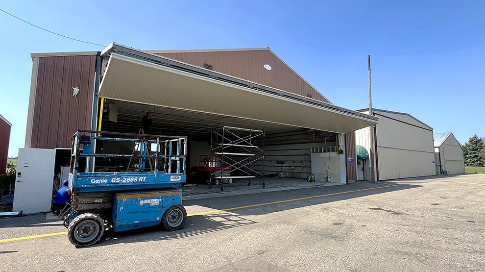 Scissor lift parked outside hangar fitted with a Schweiss bifold lift strap hangar door shown open Scissor lift parked outside hangar fitted with a Schweiss bifold lift strap hangar door shown open