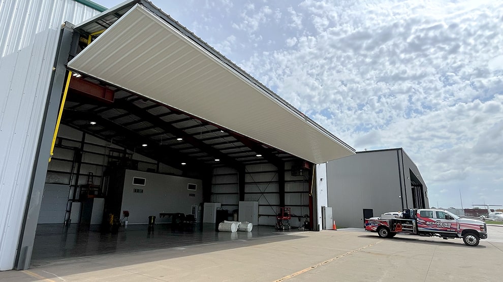 Schweiss installer truck parked outside of a hangar that has a Schweiss lift strap bifold door installed and shown open Schweiss installer truck parked outside of a hangar that has a Schweiss lift strap bifold door installed and shown open