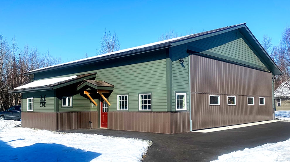 Exterior view of a green building fitted with brown Schweiss bifold liftstrap door shown closed during winter Exterior view of a green building fitted with brown Schweiss bifold liftstrap door shown closed during winter