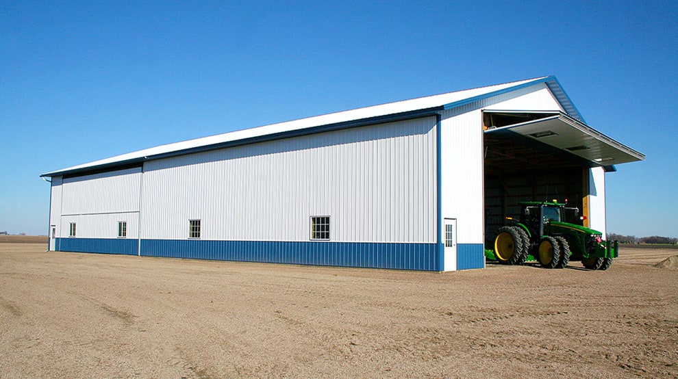 View from the left of a tractor pulling out of a farm building via the opened Schweiss bifold machine shed door View from the left of a tractor pulling out of a farm building via the opened Schweiss bifold machine shed door
