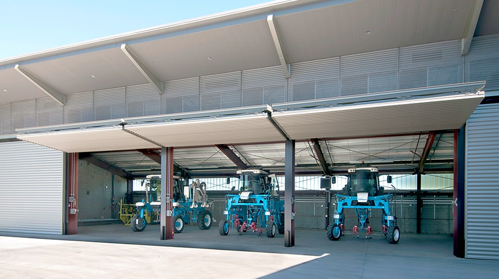 Multiple farm vehicles parked inside storage building fitted with multiple Schweiss bifold doors shown open Multiple farm vehicles parked inside storage building fitted with multiple Schweiss bifold doors shown open