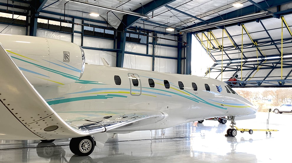 Jet parked inside hangar that is fitted with a Schweiss liftstrap bifold hangar door shown halfway open Jet parked inside hangar that is fitted with a Schweiss liftstrap bifold hangar door shown halfway open