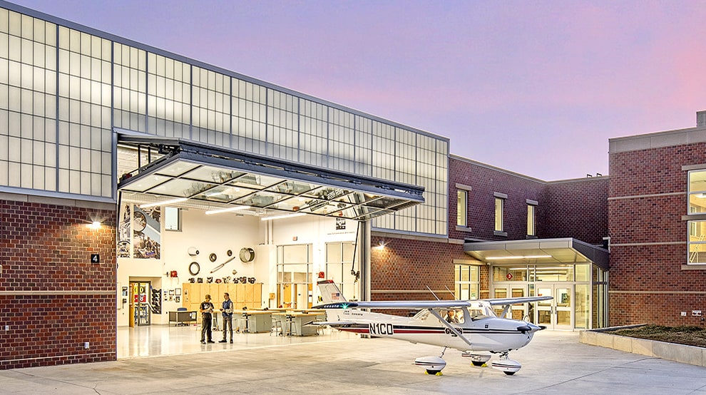 Schweiss bifold glass aviation door installed at North Star Aviation School shown open next to parked plane Schweiss bifold glass aviation door installed at North Star Aviation School shown open next to parked plane