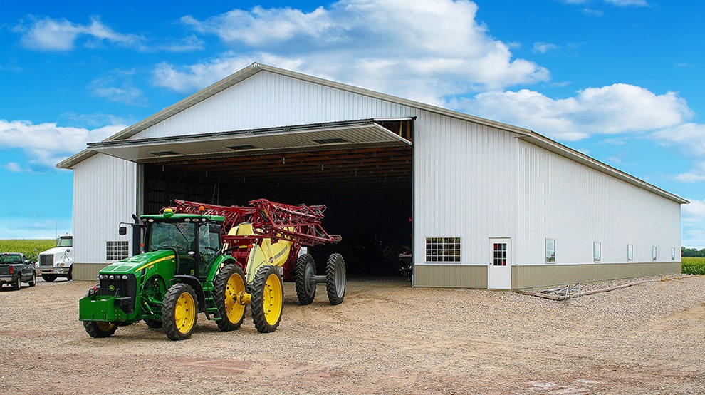 Tractor pulling farm equipment out of a agricultural storage building thats fitted with a Schweiss bifold agricultural door alt=